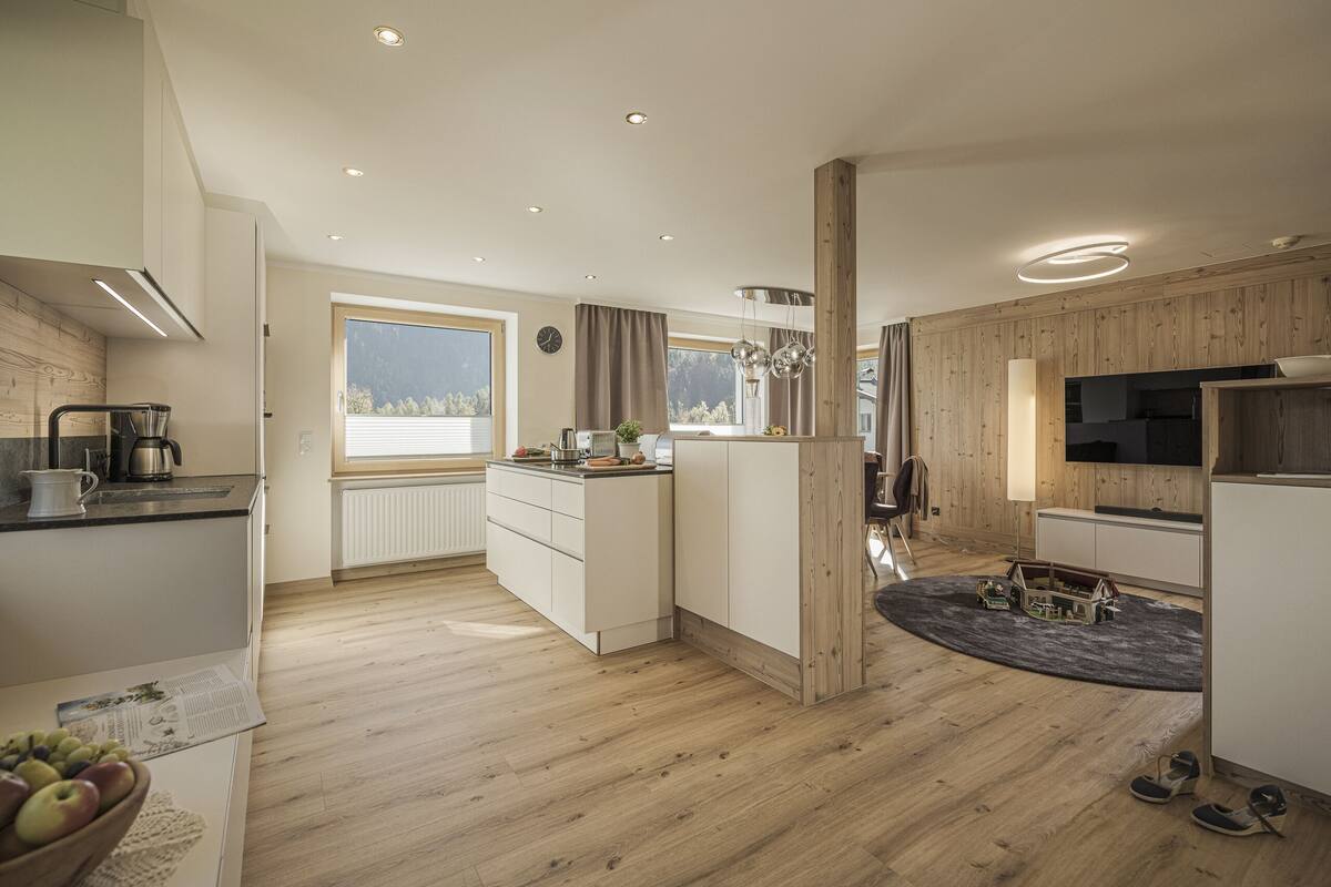 Una cocina moderna con suelo de madera, muebles blancos, horno empotrado y un ventanal que proporciona luz natural.
