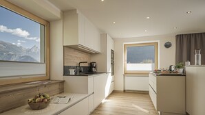 Een moderne keuken met houten vloeren, een groot raam met uitzicht op de bergen en een schaal fruit op het aanrecht.