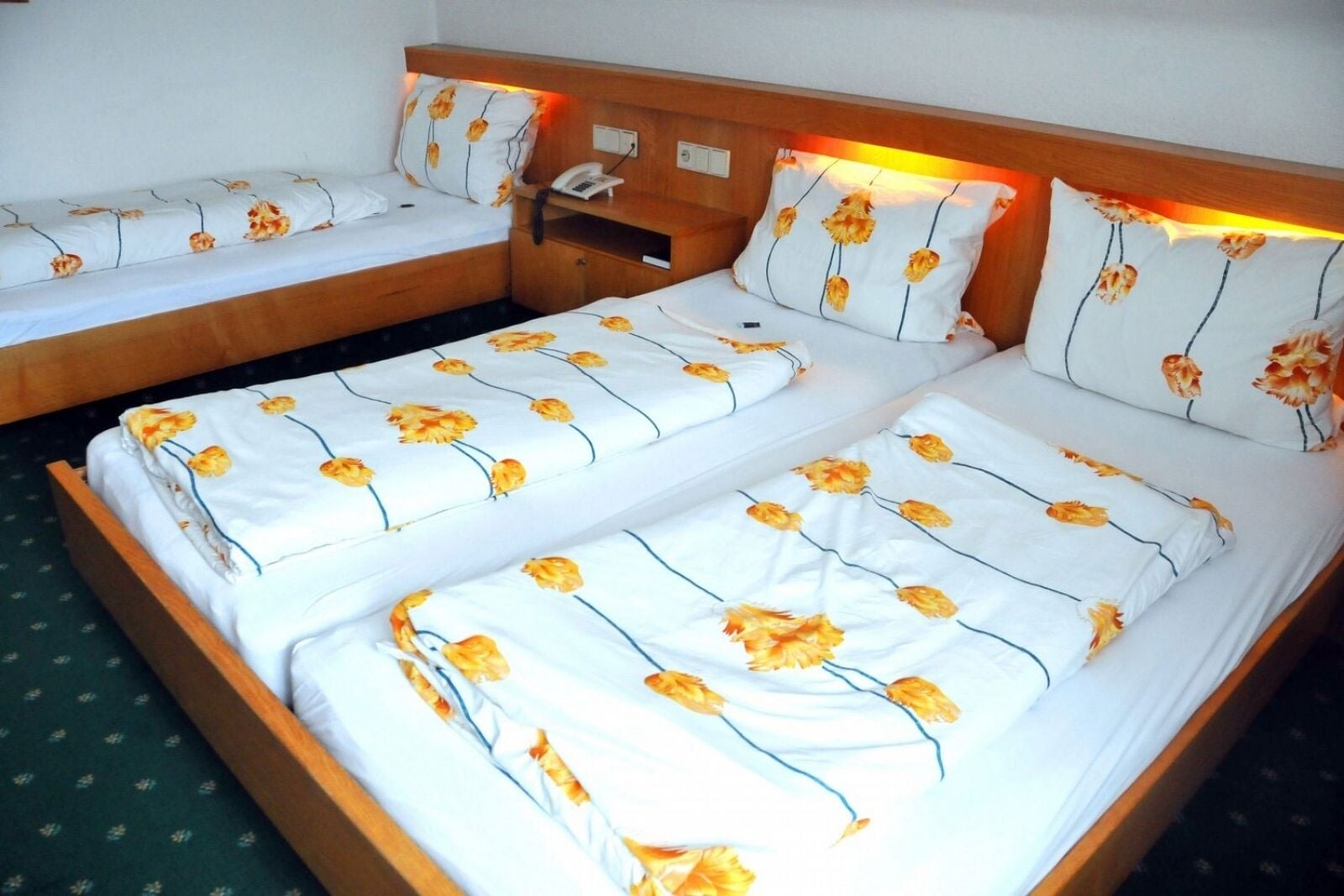 A double bed with floral bedding, a bedside table with a phone, and a nightstand.