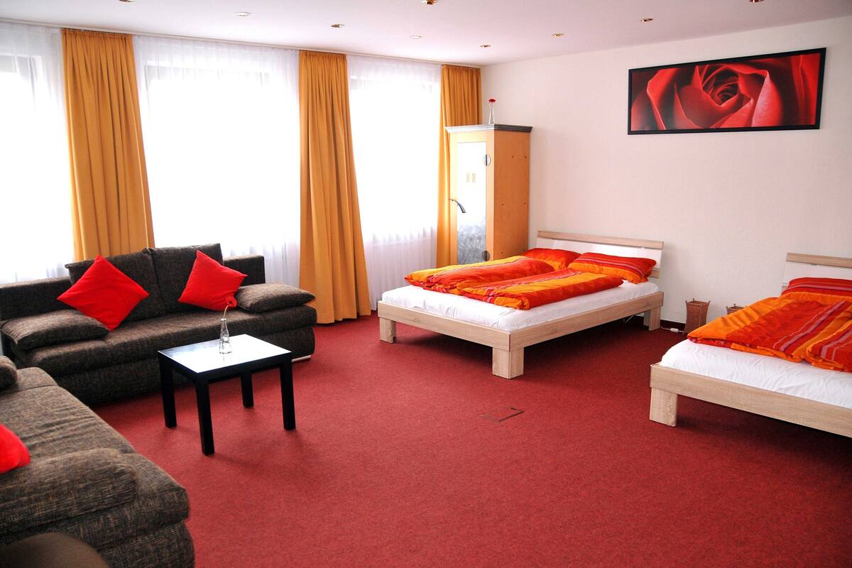 A hotel room with two beds, a sofa, a small table, and a wardrobe.