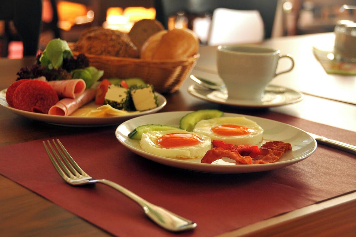 A breakfast setting with plates of food, a cup of coffee, and a basket of bread.