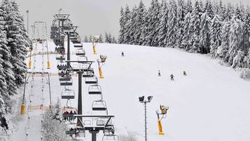Een skibaan met stoelen en een besneeuwde piste met skiërs.