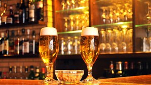 Two glasses of beer on a bar counter with a bowl of peanuts and a variety of bottles in the background. - Hotel Niedersfeld (Winterberg)