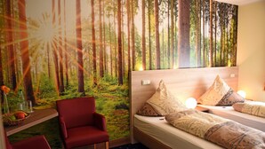 A room with a bed, red chairs, a shelf with fruits, and a forest mural on the wall. - Hotel Niedersfeld (Winterberg)
