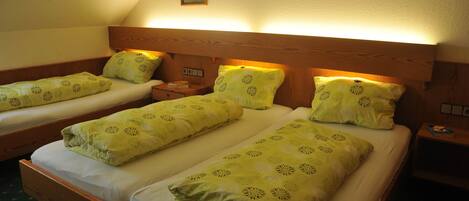 Habitación con tres camas individuales, cada una con cabecero de madera y ropa de cama estampada en verde. Se observan mesitas de noche con lámparas y una lámpara de pared sobre las camas.