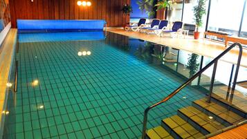 Une piscine intérieure dotée d’un banc bleu rembourré, de chaises longues et d’une terrasse en bois avec des marches menant à l’eau.