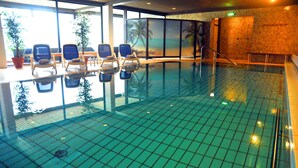 An indoor swimming pool with a tiled floor, lounge chairs, and a mural of a beach scene. - Hotel Niedersfeld (Winterberg)