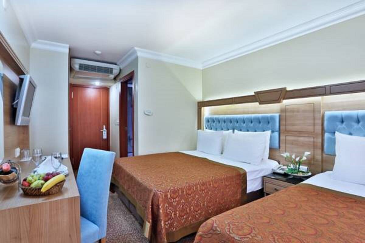 A hotel room with two beds, a desk with a fruit bowl, a chair, and a television.
