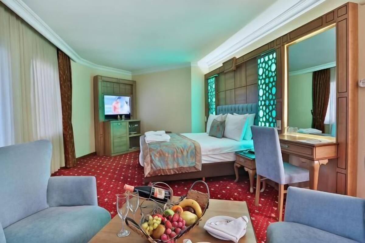 A hotel room with a bed, a desk, a chair, a TV, and a fruit basket.