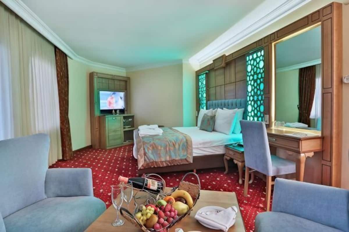 Habitación de hotel con cama, escritorio, silla, televisor y cesta de frutas.