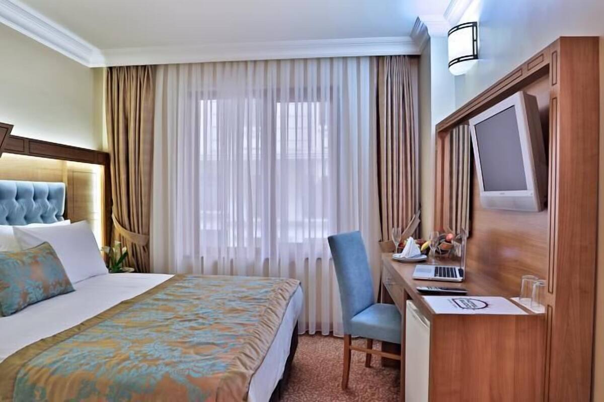 A hotel room with a bed, a desk with a laptop, a TV, and a chair.