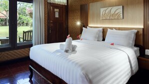 Une chambre d’hôtel avec un grand lit, une tête de lit en bois, un ventilateur de plafond et une vue sur l’extérieur.