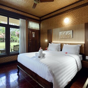Une chambre d’hôtel avec un grand lit, une tête de lit en bois, un ventilateur de plafond et une vue sur l’extérieur.