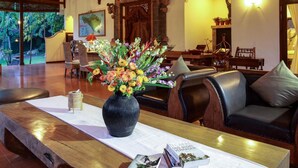 Une pièce spacieuse avec un plafond en bois, une table à manger agrémentée d’un vase de fleurs, des sièges en cuir et une vue sur l’extérieur.