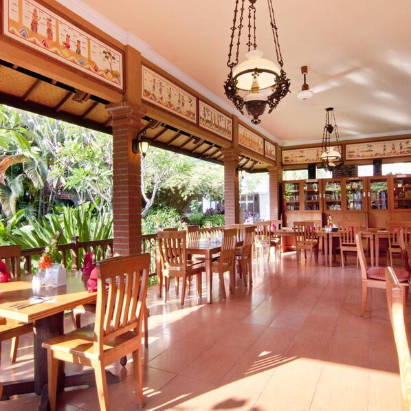 Un restaurant avec des meubles en bois, des luminaires suspendus et une vue sur la verdure environnante.