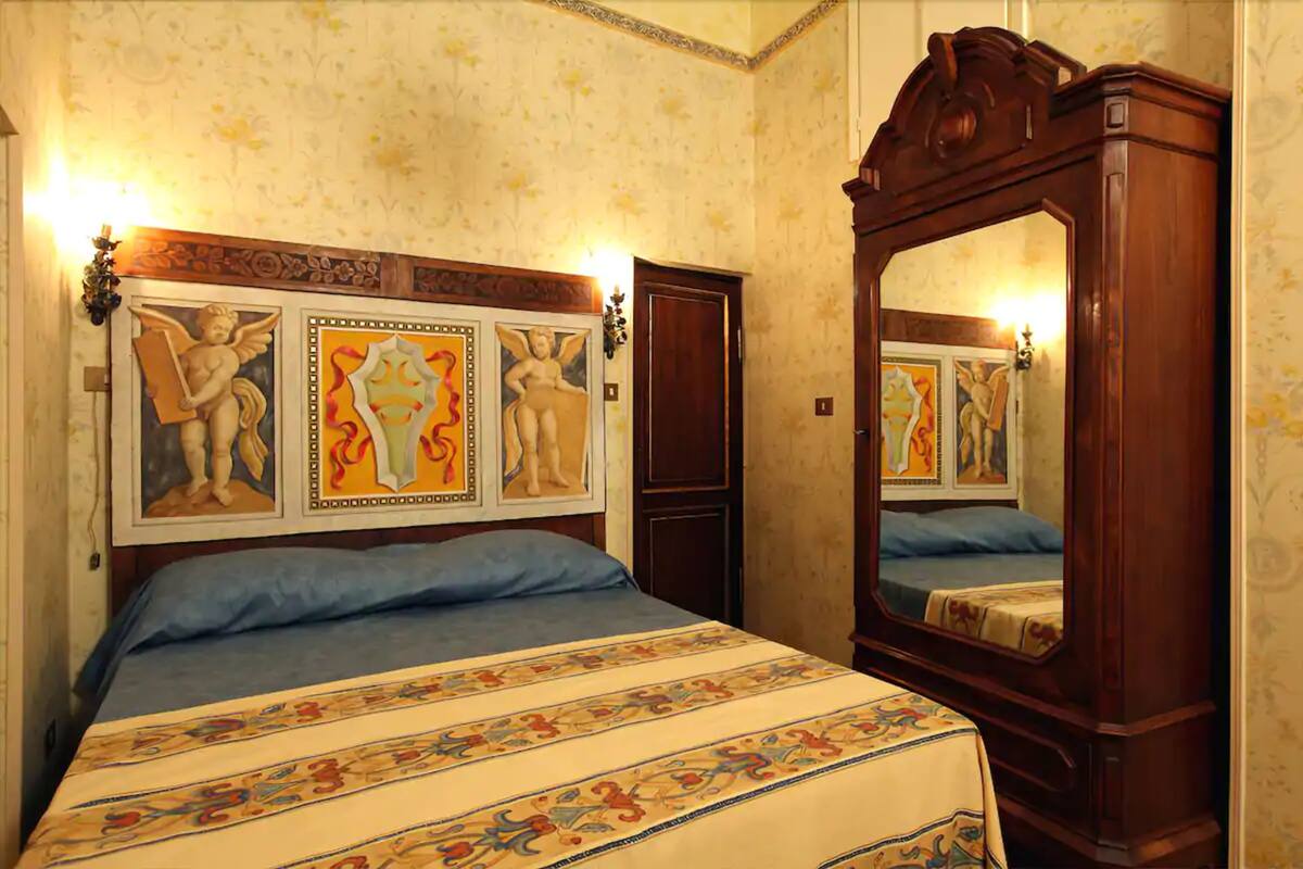A bedroom with a large bed, a wooden wardrobe, and a mirror.
