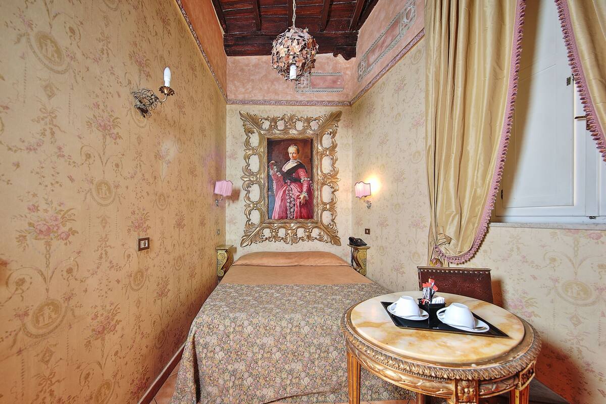 A room with a bed, a round table with cups, a mirror, and a chandelier.