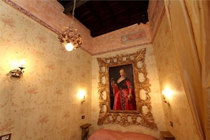 Una habitación con papel tapiz floral, un espejo grande y ornamentado, y una cama con cubrecama rojo.