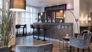 Hall d'ingresso di un hotel moderno con zona bar, posti a sedere e una pianta grande.