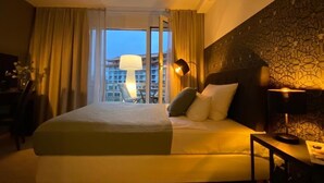Camera d'albergo con un letto grande, una scrivania, una sedia, una lampada e vista su un edificio dalla finestra.
