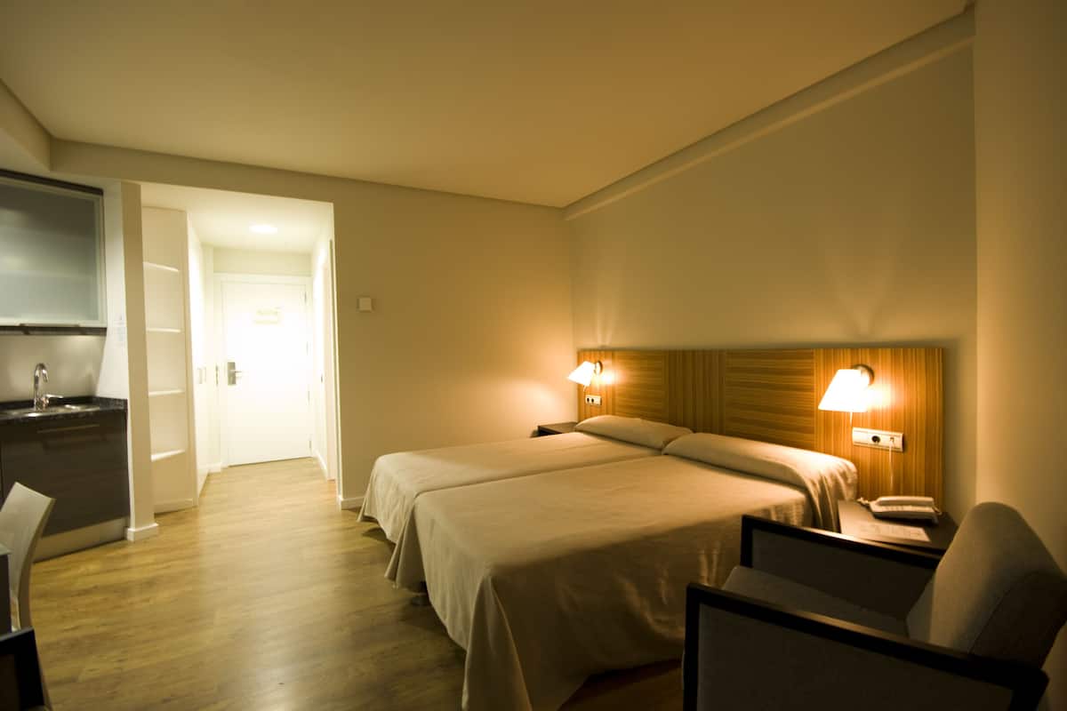 A hotel room with two beds, a desk, a chair, and a TV.
