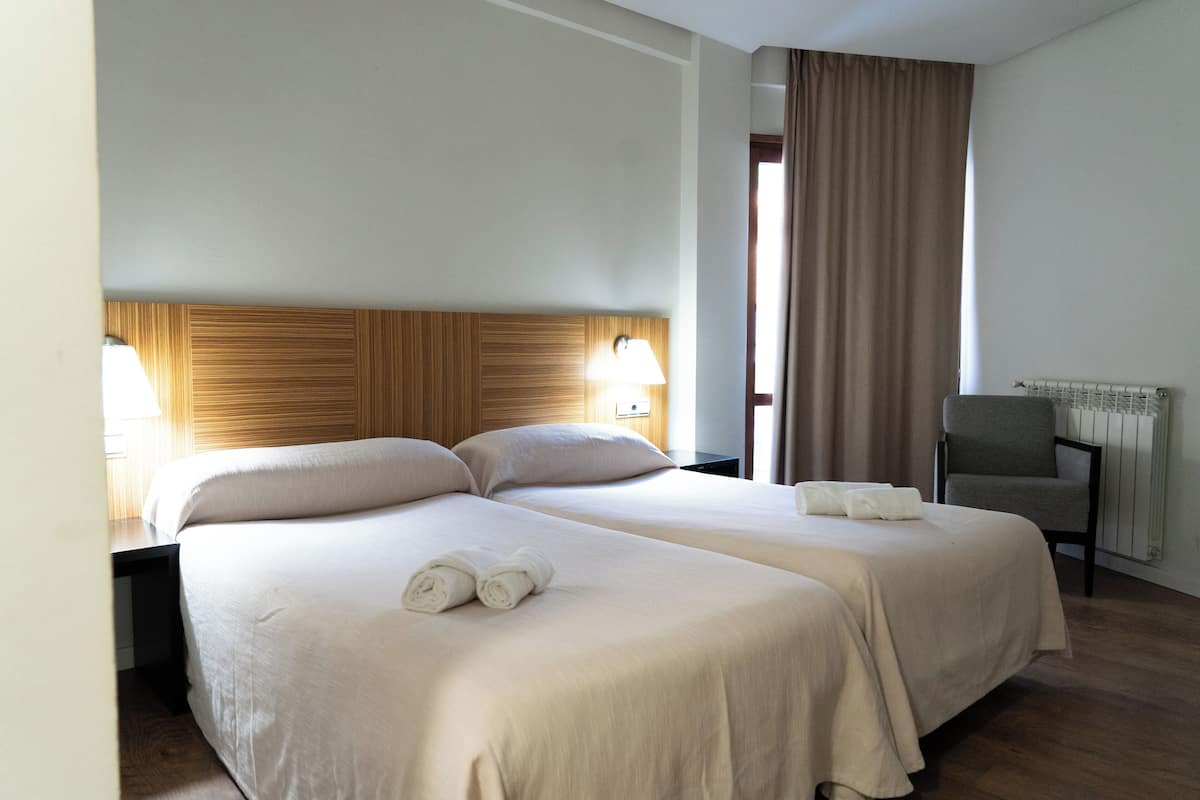 Une chambre d’hôtel avec deux lits, une tête de lit en bois, un bureau, une chaise et un radiateur.