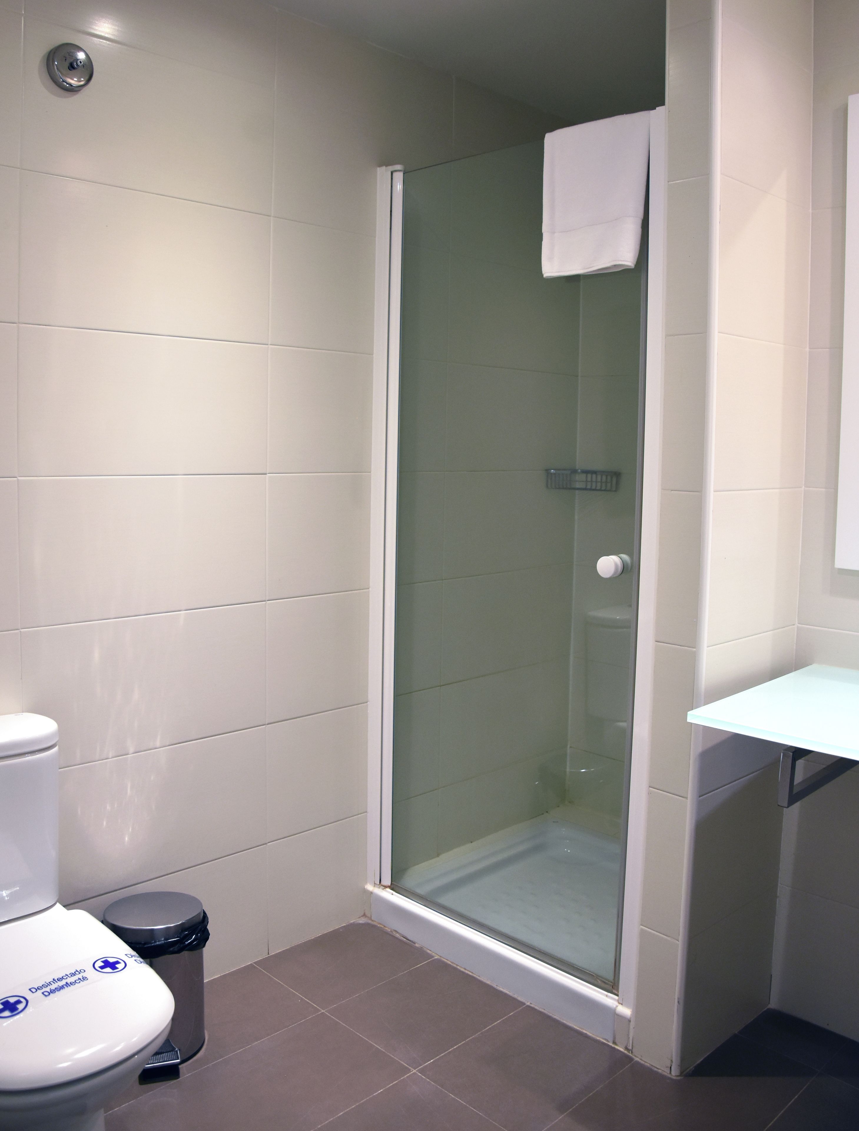 A bathroom with a toilet, a trash bin, a glass shower enclosure, and a white sink.