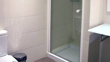 A bathroom with a toilet, a trash bin, a glass shower enclosure, and a white sink.