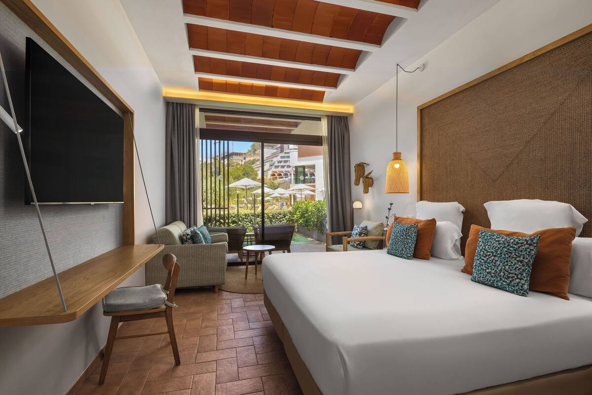 Une chambre d’hôtel avec un grand lit, un canapé, une petite table et un téléviseur fixé au mur.