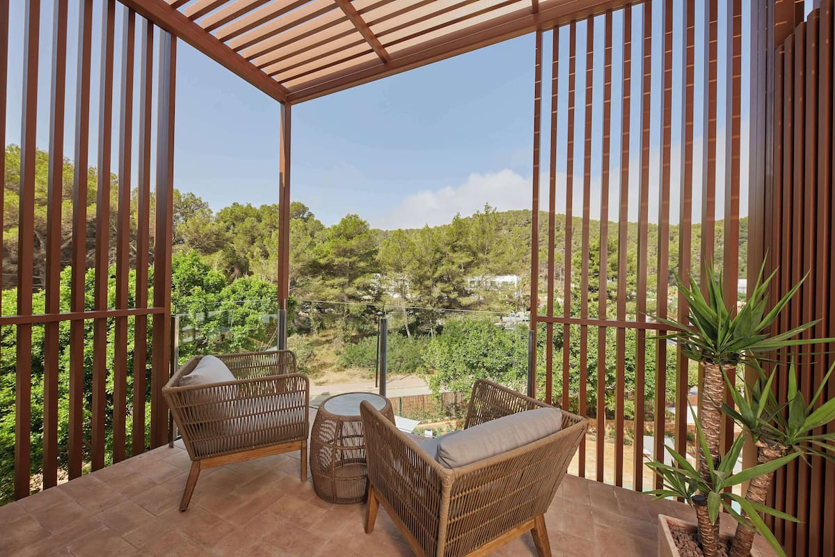 Une terrasse couverte, meublée de meubles en osier, offrant une vue sur un paysage boisé.