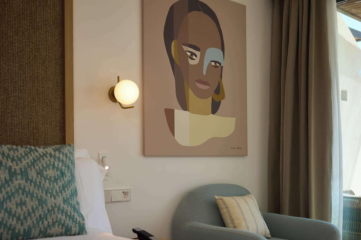 Une chambre d’hôtel avec un lit, une chaise, une lampe fixée au mur et un tableau.