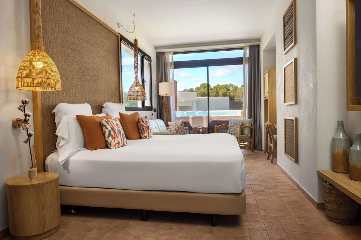 Une chambre d’hôtel avec un grand lit, une table de chevet, une lampe et une vue sur l’extérieur.