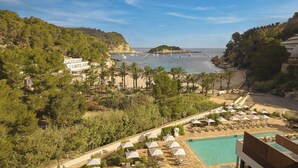 A resort with a pool, beach, and boats in the background. - Cala San Miguel Ibiza Resort, Curio Collection by Hilton (Sant Joan de Labritja)