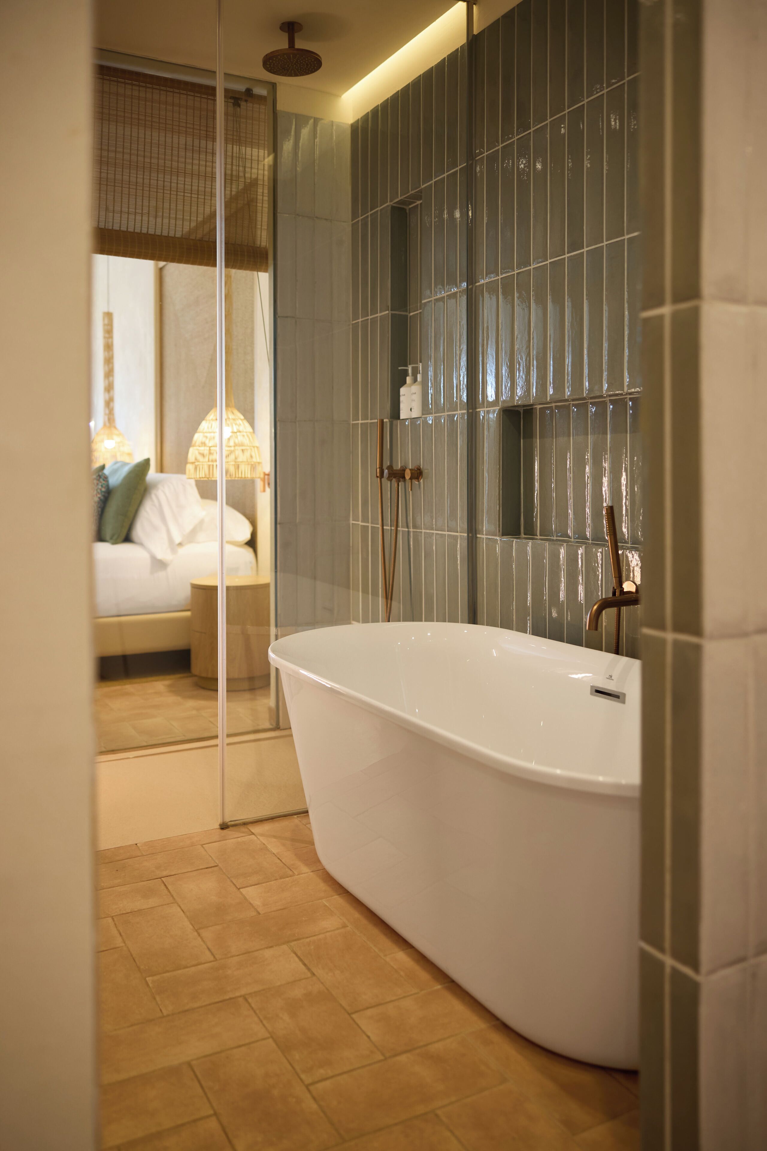 A modern bathroom with a freestanding bathtub, a glass shower enclosure, and a visible bedroom with a bed and a nightstand.