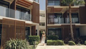 A modern building with a central courtyard, a palm tree, and a person walking. - Cala San Miguel Ibiza Resort, Curio Collection by Hilton (Sant Joan de Labritja)