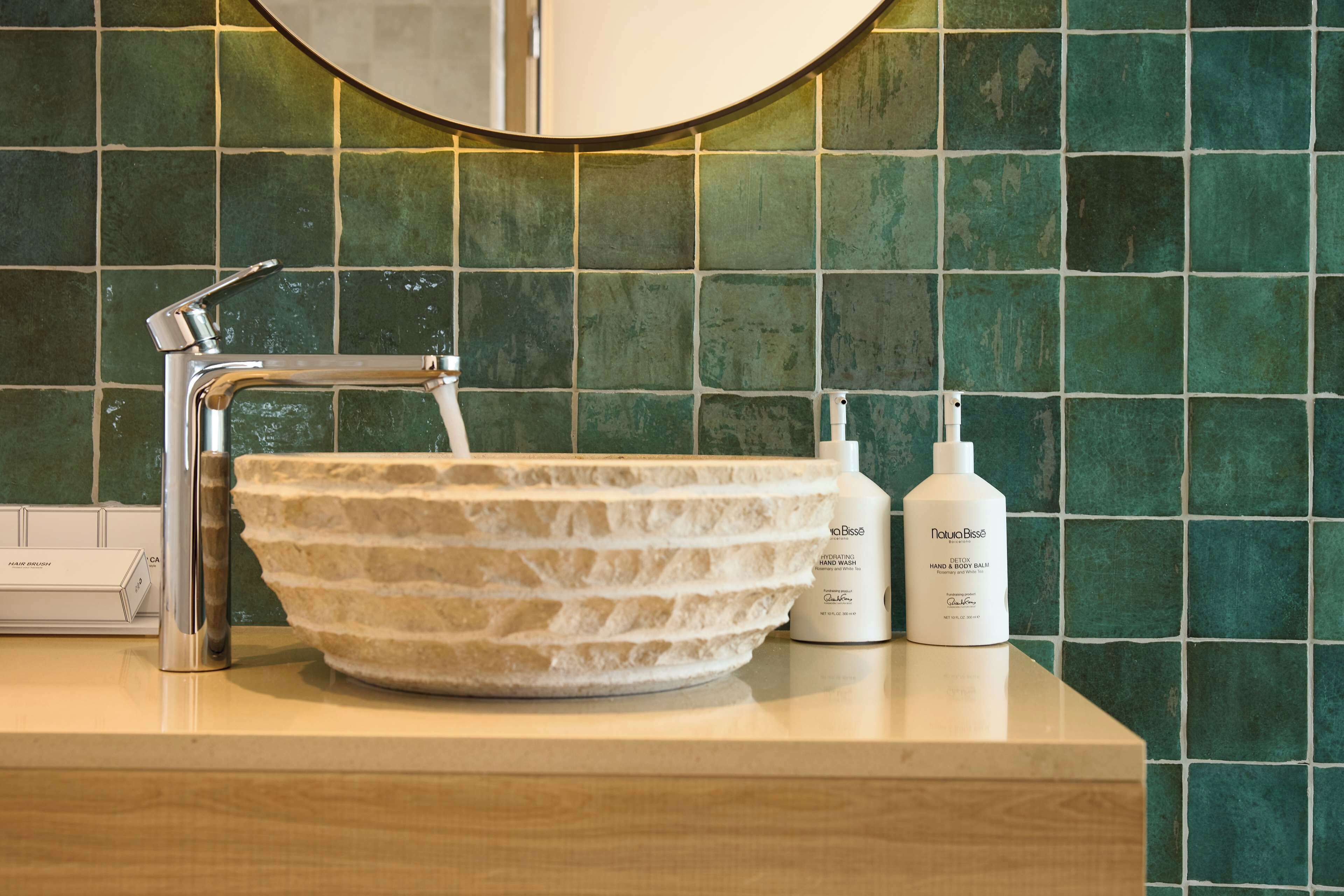 A bathroom with a stone sink, a modern faucet, and two bottles of hand soap on the counter.