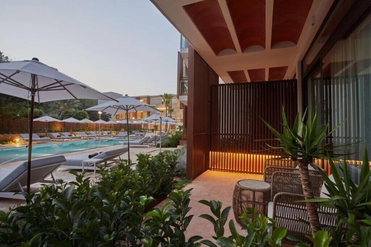 Un espace aménagé au bord de la piscine, avec des chaises longues et des parasols, une piscine, et un coin salon doté de meubles en osier.