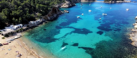 A coastal area with clear turquoise waters, boats, and a beach with people.