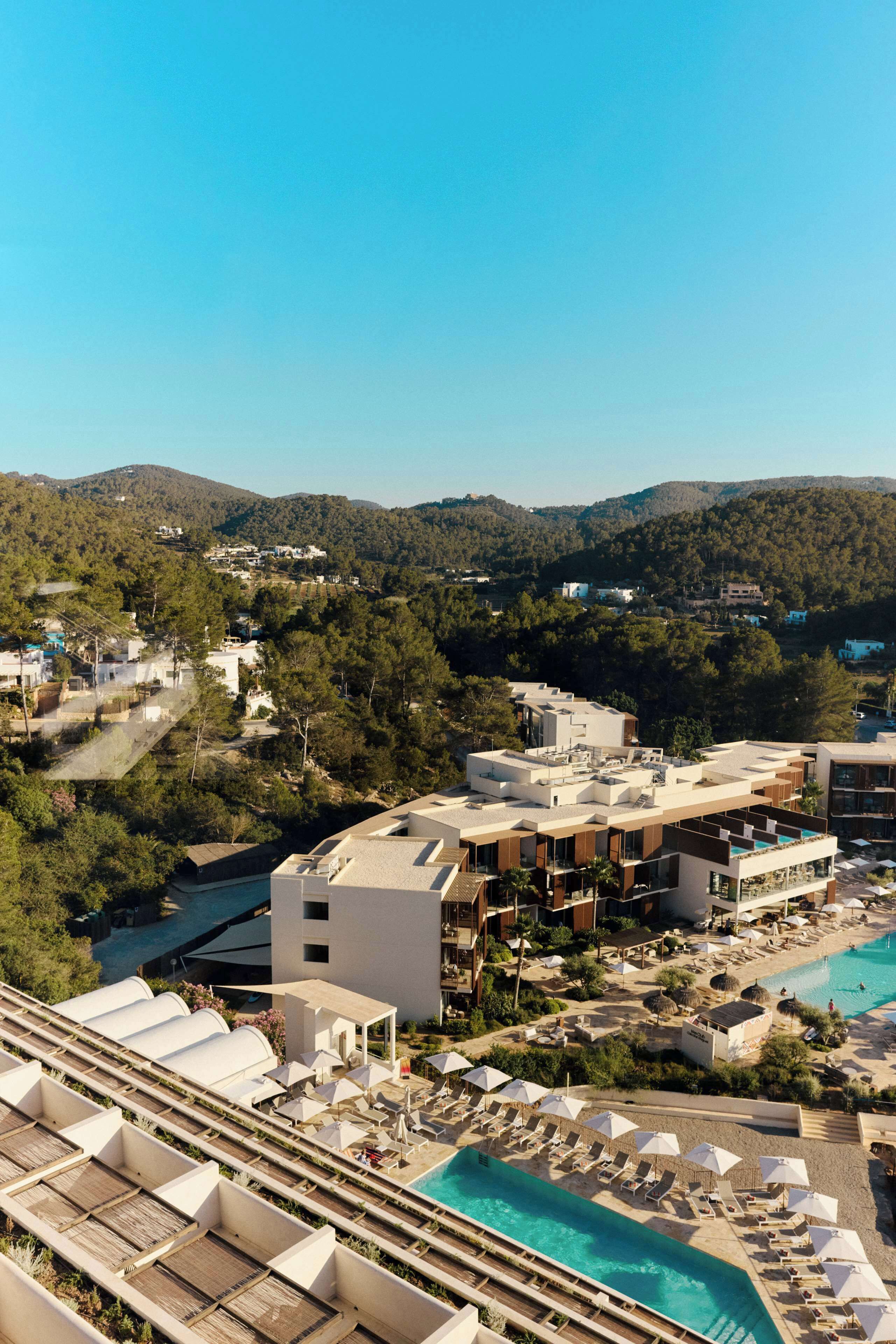 A resort with a swimming pool, sun loungers, and a view of the surrounding hills.