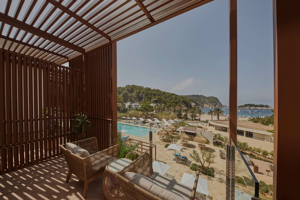 Un balcon agrémenté de meubles en osier, une piscine et une vue sur une plage et des montagnes.
