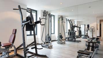 Un gimnasio con diversas máquinas de ejercicio, amplias ventanas y un espejo que refleja los equipos.