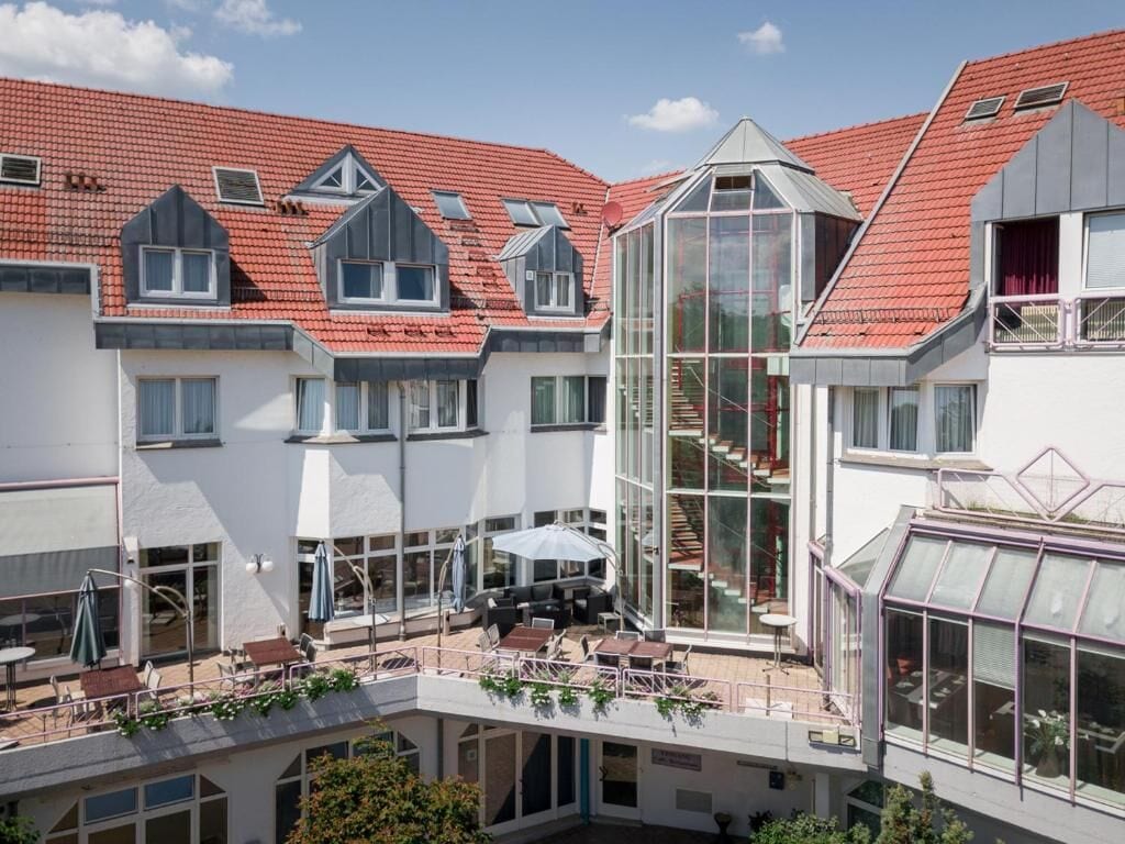 A multi-story building with a red-tiled roof, large glass windows, and outdoor seating areas.