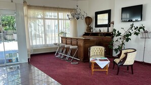 A spacious room with a red carpet, a chandelier, a wooden cabinet, a television, and a potted plant. - Hotel Aichtaler Hof (Aichtal)