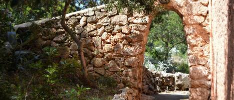 A stone archway leading through a natural landscape with trees and shrubs.