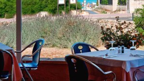 Un área de comedor al aire libre con sillas y mesas, con vista a una playa donde se ven personas a lo lejos.