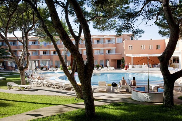 Zona de piscina con sillas de descanso y un edificio con balcones al fondo.
