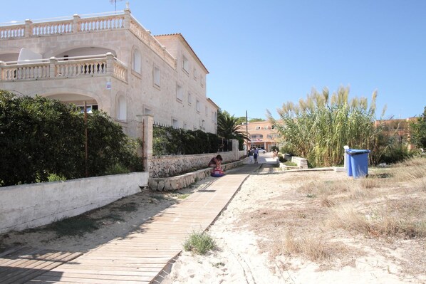 Un paseo marítimo con un muro de piedra, una pasarela de madera y un edificio con balcón.