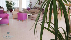 Un amplio vestíbulo de hotel con muebles modernos, una planta grande y el logotipo visible de 'XALOC Playa Hotel'.