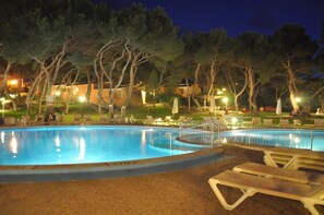 A swimming pool surrounded by lounge chairs and trees, with buildings in the background. - Hotel Xaloc Playa (Sant Lluis)