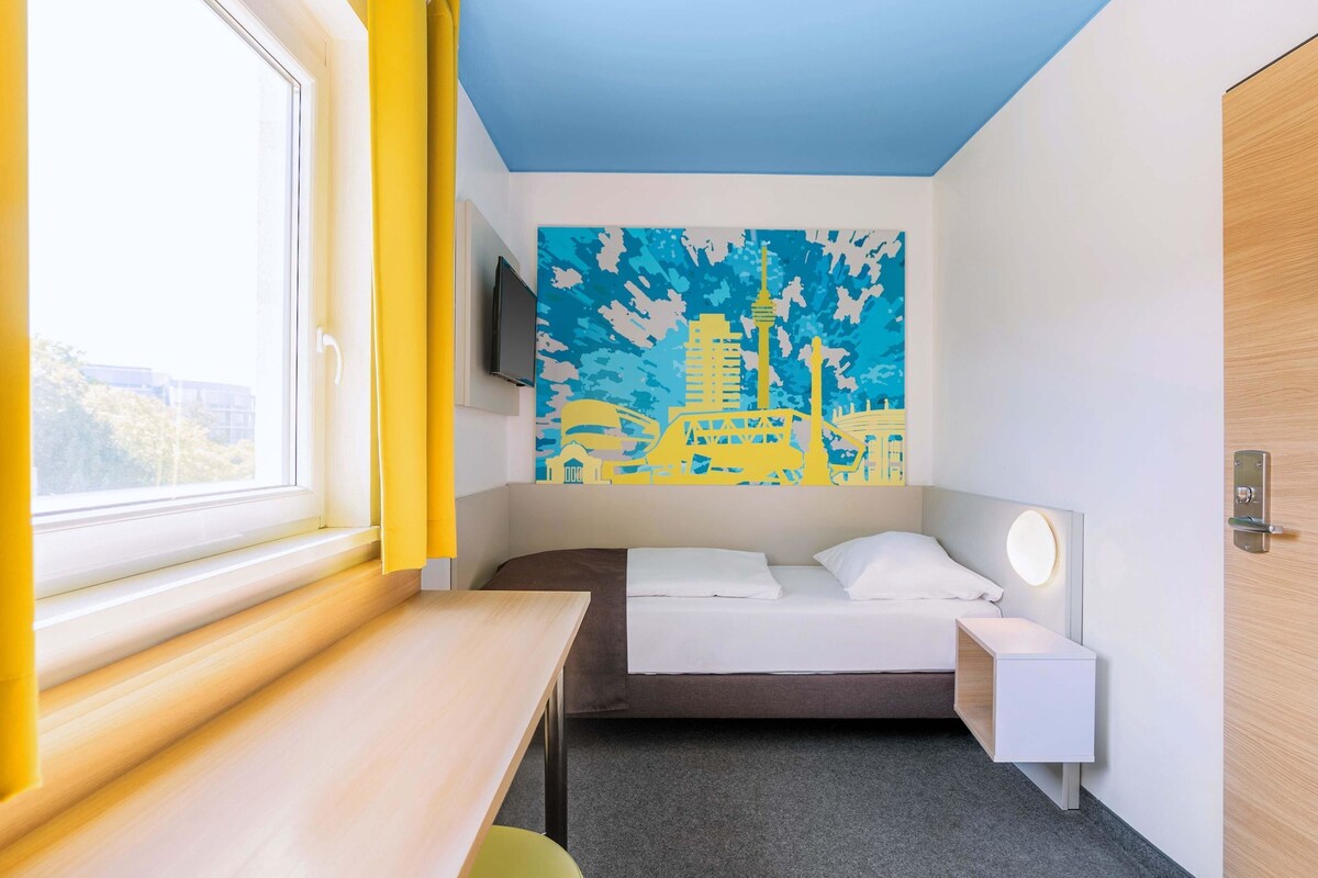 A hotel room with a bed, bedside table, and a large window.